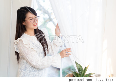 Portrait of Happy Attractive asian people cute woman wearing white lace shirt with the curtains on the window in the room felt like relaxing in house like the background 127701743