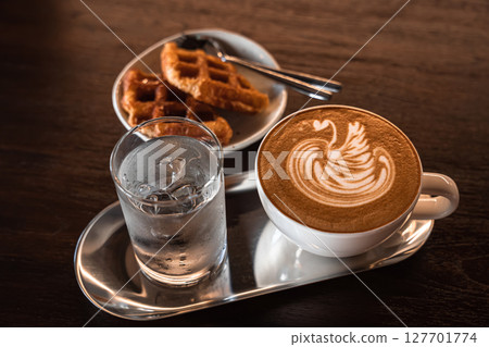Hot coffee latte with latte art milk foam in a swan shape in cup mug and Homemade Belgian Waffles with honey on wood desk on top view. As breakfast In a coffee shop at the cafe,during business work. 127701774