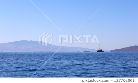 A calm blue sea with a traditional sailing boat in the distance, against a backdrop of hazy mountains and a clear sky. High quality photo A calm blue sea with a traditional sailing boat in the distance, against a backdrop of hazy mountains and a clear sky. High quality photo 127702001