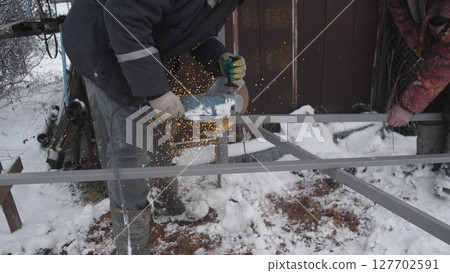 A skilled worker fabricates metal in harsh snowy conditions, showcasing expertise in winter metalworking 127702591