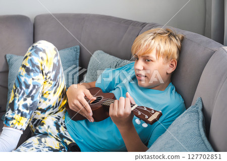 Teenager Lying on Sofa Playing the Ukulele. Relaxing at Home by Making Music. 127702851