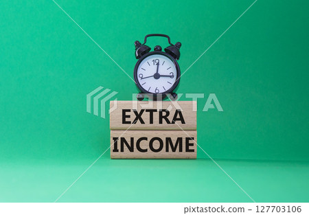 Extra Income symbol. Concept words Extra Income on wooden blocks. Beautiful green background with alarm clock. Business and Extra Income concept. Copy space. Extra Income symbol. Concept words Extra Income on wooden blocks. Beautiful green background with alarm clock. Business and Extra Income concept. Copy space. 127703106