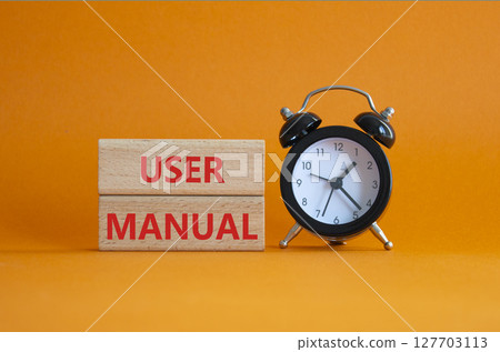 User Manual symbol. Concept words User Manual on wooden blocks. Beautiful orange background with alarm clock. Business and User Manual concept. Copy space. 127703113