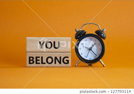 You belong symbol. Concept words You belong on wooden blocks. Beautiful orange background with alarm clock. Business and You belong concept. Copy space. 127703114
