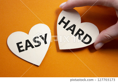 Easy or Hard symbol. Concept word Easy or Hard on wooden hearts. Businessman hand. Beautiful orange background. Business and Easy or Hard concept. Copy space 127703173