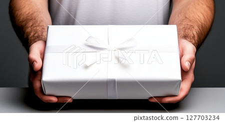 Gift-wrapped present held by a person with hands in a neutral setting, showcasing a surprise for an upcoming celebration or special occasion 127703234