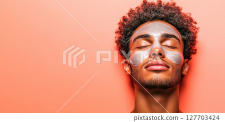 Man relaxing with face mask on smooth skin against coral background in cozy indoor setting during afternoon relaxation time 127703424