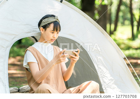 一個女孩在露營地的帳篷前看著她的智慧型手機 一個女孩在露營地的帳篷前看著她的智慧型手機 127703708