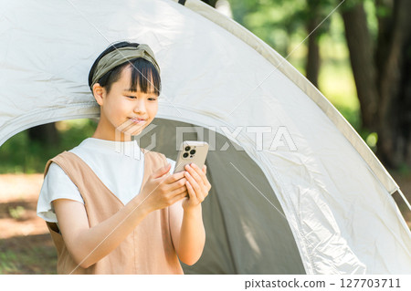 A girl looking at her smartphone in front of a tent at a campsite 127703711