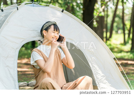 A girl talking on a smartphone in front of a tent at a campsite A girl talking on a smartphone in front of a tent at a campsite 127703951