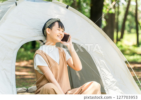 一個女孩在露營地的帳篷前用智慧型手機聊天 127703953