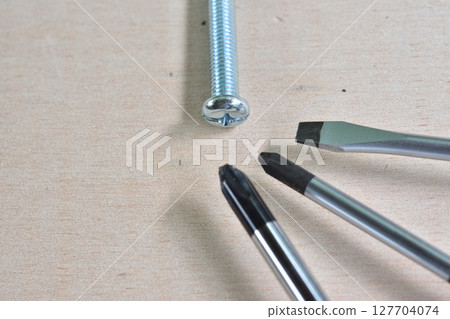 Screws and a screwdriver placed on a wooden board 127704074
