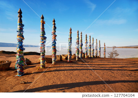 Wooden ritual pillars with multicolored ribbons . Lake Baikal on a sunny spring day, Olkhon Island. 127704104