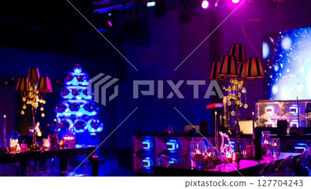 A dark, large room decorated for a festive event, featuring candelabras with patterned shades, and a prominent blue, illuminated disco ball Christmas tree. A dark, large room decorated for a festive event, featuring candelabras with patterned shades, and a prominent blue, illuminated disco ball Christmas tree. 127704243