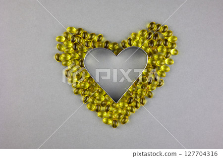 Gel yellow capsules with vitamin D3 on a gray background, laid out in the shape of a heart. 127704316