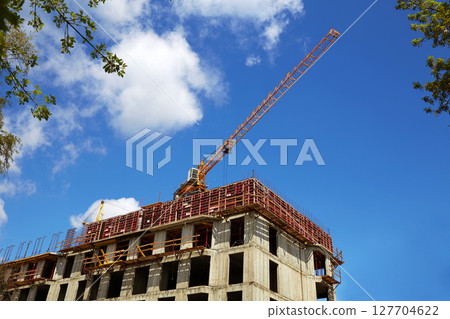 Crane on the building site. Construction of an apartment building, blue sky. 127704622