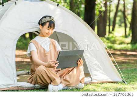 一個女孩在露營地/休閒設施的帳篷裡使用平板電腦 一個女孩在露營地/休閒設施的帳篷裡使用平板電腦 127705365
