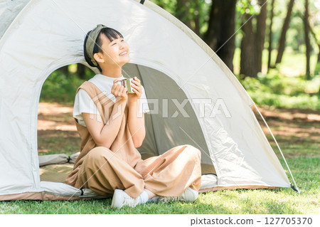 A girl drinking a drink in front of a tent at a campsite or leisure facility 127705370