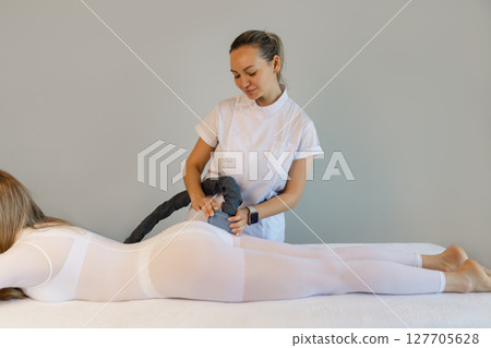 Woman in special white suit getting anti cellulite massage in a spa salon. LPG, and body contouring treatment in clinic.Reset body weight with LPG massage.  127705628