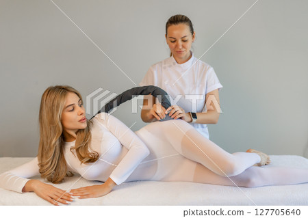 Woman in special white suit getting anti cellulite massage in a spa salon. LPG, and body contouring treatment in clinic.Reset body weight with LPG massage.  127705640