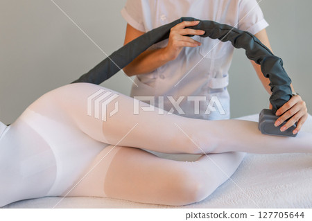 Woman in special white suit getting anti cellulite massage in a spa salon. LPG, and body contouring treatment in clinic.Reset body weight with LPG massage.  127705644