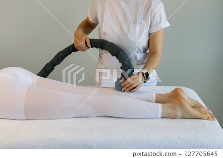 Woman in special white suit getting anti cellulite massage in a spa salon. LPG, and body contouring treatment in clinic.Reset body weight with LPG massage. Woman in special white suit getting anti cellulite massage in a spa salon. LPG, and body contouring treatment in clinic.Reset body weight with LPG massage. 127705645