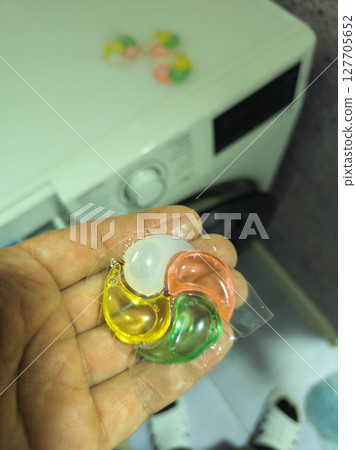 Adult man holding laundry detergent pod in bathroom at night 127705652