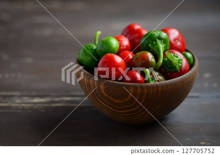 Freshly harvested red and green chili peppers arranged in a rustic wooden bowl on a dark wooden surface, showcasing vibrant colors and textures Freshly harvested red and green chili peppers arranged in a rustic wooden bowl on a dark wooden surface, showcasing vibrant colors and textures 127705752