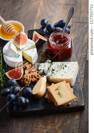 Assorted gourmet cheese platter featuring figs, grapes, honey, and crackers arranged on a wooden board for an elegant dining experience Assorted gourmet cheese platter featuring figs, grapes, honey, and crackers arranged on a wooden board for an elegant dining experience 127705753