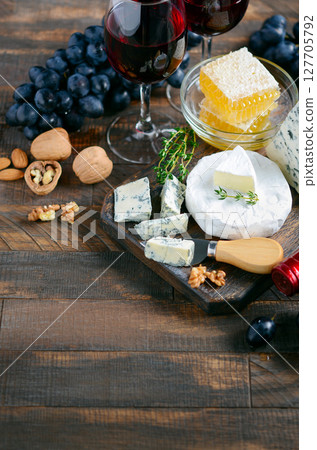 Assorted gourmet cheeses, red wine glasses, fresh grapes, and nuts arranged on a wooden table, creating an inviting culinary experience Assorted gourmet cheeses, red wine glasses, fresh grapes, and nuts arranged on a wooden table, creating an inviting culinary experience 127705792