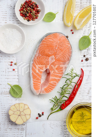 Fresh salmon steak surrounded by herbs, spices, and lemon slices on a rustic wooden surface, showcasing vibrant colors and culinary potential 127705807