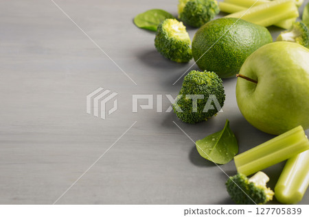 Fresh green vegetables including broccoli, celery, and green apple arranged artistically on a textured gray surface, showcasing healthy eating concepts 127705839
