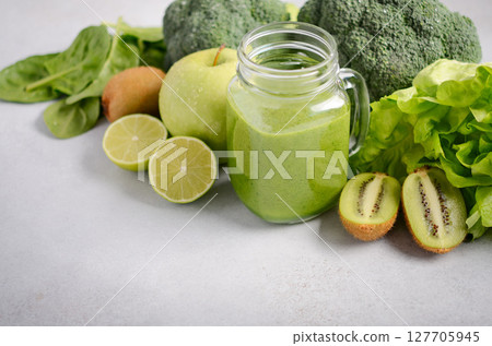 Green smoothie in a glass jar surrounded by fresh vegetables and fruits, showcasing healthy lifestyle choices and vibrant nutrition options 127705945