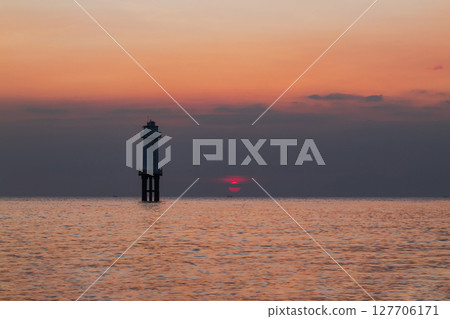 White lighthouse structure stands in the tranquil sea at golden hour sunset 127706171