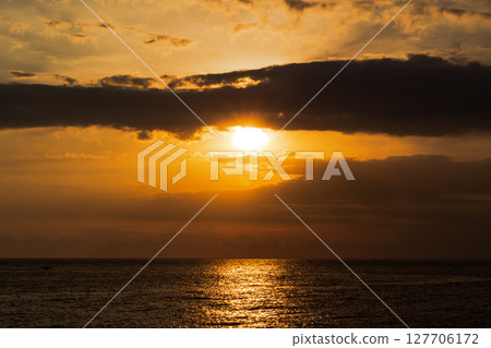Golden sunset light reflects beautifully on dark ocean waves under dramatic clouds 127706172
