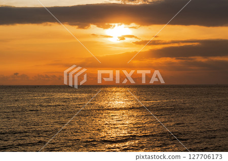 Golden sunset light reflects beautifully on dark ocean waves under dramatic clouds 127706173
