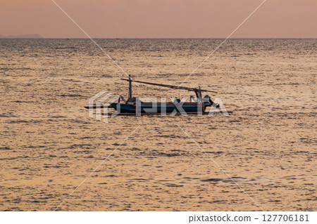 Small traditional boat sailing peacefully on calm ocean water at golden hour 127706181