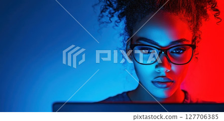 Engaging young woman working on a laptop with colorful lighting during a late-night study session at home 127706385