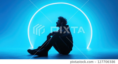 Creative contemplative moment captured with a silhouette against a vibrant blue neon backdrop during an artistic photoshoot 127706386