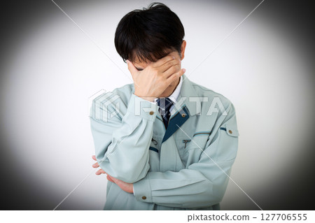 A worried middle-aged male businessman wearing green work clothes 127706555