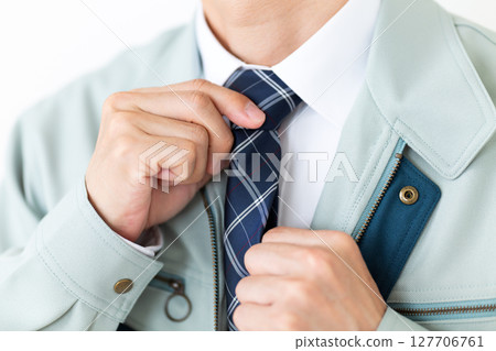 A middle-aged male businessman wearing green work clothes and tying a tie 127706761