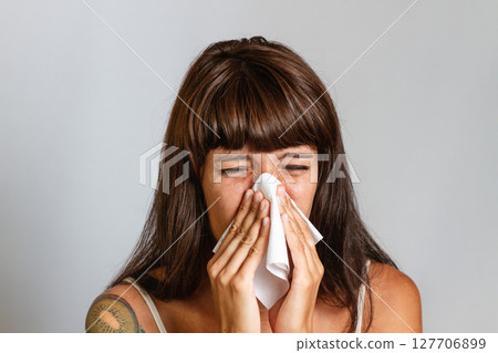 Colds and seasonal viral diseases. A brunette woman sneezes or blows her nose in a handkerchief. Copy space 127706899