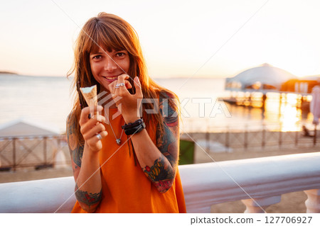 Portrait of young happy beautiful Caucasian woman with tattoos holds ice cream and looking at camera. Concept of freedom and psychology Portrait of young happy beautiful Caucasian woman with tattoos holds ice cream and looking at camera. Concept of freedom and psychology 127706927