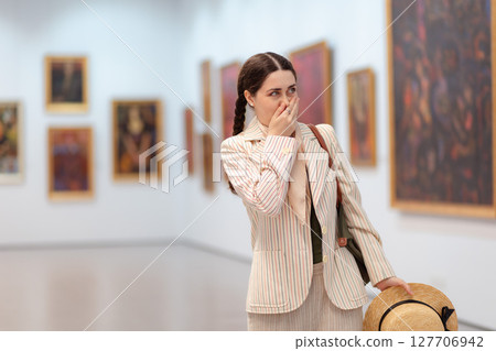 Mid shot a young elegant Caucasian woman experiences embarrassment when visiting a contemporary art exhibition. The concept of the Museum Day Mid shot a young elegant Caucasian woman experiences embarrassment when visiting a contemporary art exhibition. The concept of the Museum Day 127706942