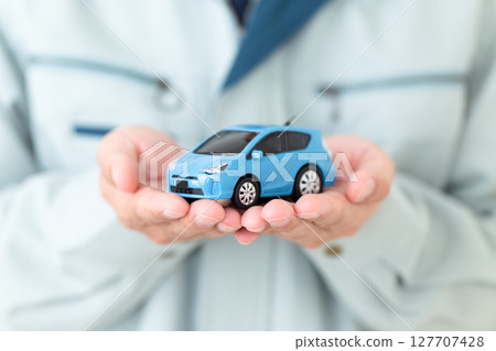 A middle-aged male businessman wearing green work clothes and holding a miniature car A middle-aged male businessman wearing green work clothes and holding a miniature car 127707428