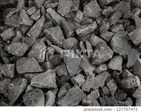 A close-up view of a textured background made of small, irregularly shaped dark gray stones. A close-up view of a textured background made of small, irregularly shaped dark gray stones. 127707472