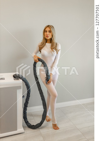 Woman in white suit for LPG massage. Anti-cellulite body care concept. Gray background Woman in white suit for LPG massage. Anti-cellulite body care concept. Gray background 127707501