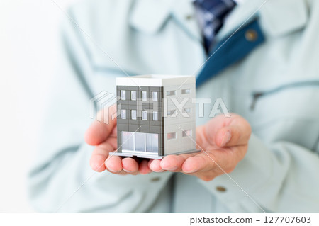 A middle-aged male businessman wearing green work clothes and holding a miniature building 127707603
