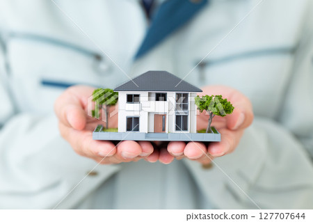 A middle-aged male businessman wearing green work clothes and holding a miniature house A middle-aged male businessman wearing green work clothes and holding a miniature house 127707644
