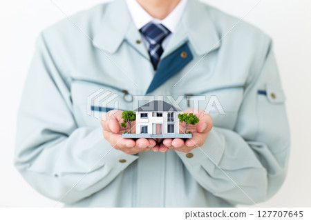 A middle-aged male businessman wearing green work clothes and holding a miniature house 127707645